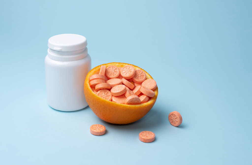 White bottle and orange tablets of vitamin C with half an orange on a blue background, mockup.